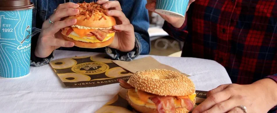 Couple eating Einstein Bros. bagel egg sandwiches with coffee