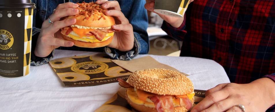 Couple eating Einstein Bros. bagel egg sandwiches with coffee