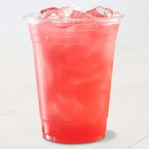 A clear plastic cup filled with a vibrant red, iced beverage sits on a light surface. The drink appears refreshing.