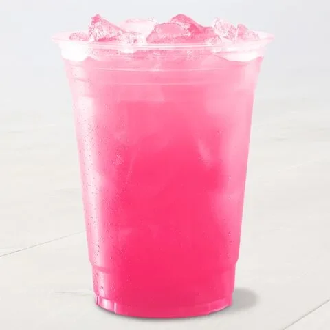 A clear plastic cup filled with a vibrant pink, iced beverage sits on a light surface. The drink appears refreshing.
