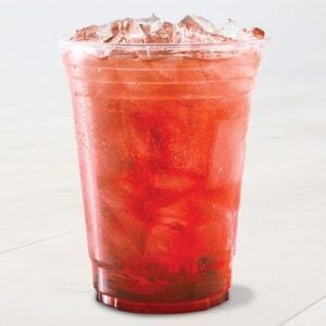 A clear plastic cup filled with a deep red, iced beverage sits on a light surface. The drink appears refreshing.