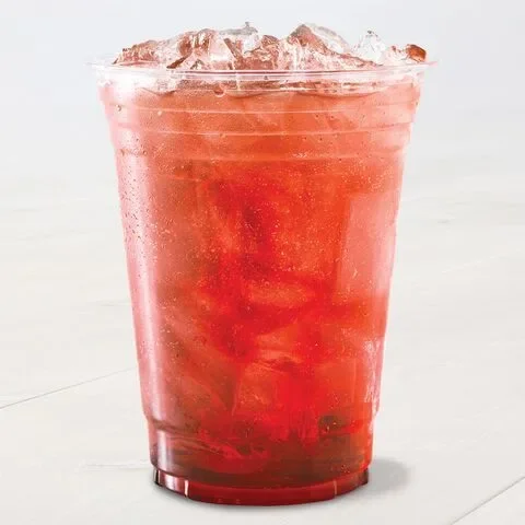 A clear plastic cup filled with a deep red, iced beverage sits on a light surface. The drink appears refreshing.