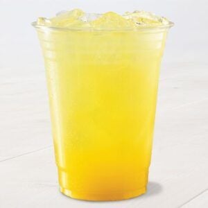 A clear plastic cup filled with a bright yellow, iced beverage sits on a light surface. The drink appears refreshing.