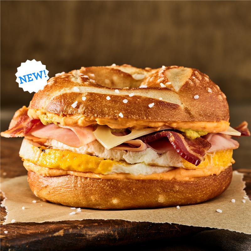 Close-up of Einstein Bros. Bagels Oktoberfest Egg Sandwich with melty Swiss cheese, egg, and ham and bacon topped with creamy beer cheese and spicy brown mustard